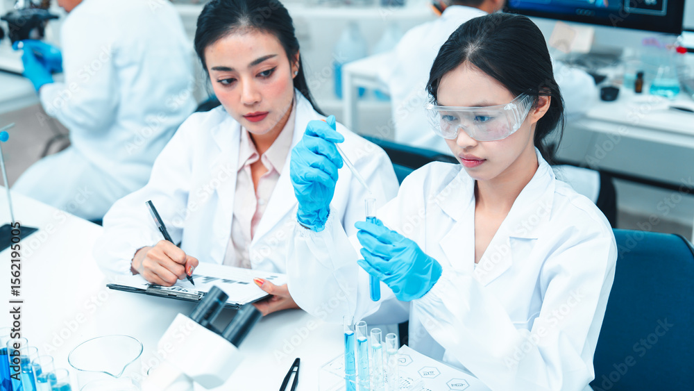 Two female scientists working in a modern laboratory. One is carefully transferring liquid with a pipette while the other observes and takes notes. STEM education and teamwork in a research setting. Two female scientists working in a modern laboratory. One is carefully transferring liquid with a pipette while the other observes and takes notes. STEM education and teamwork in a research setting.
