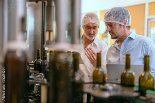 Two professionals discussing wine bottling process inside a modern winery facility in the afternoon