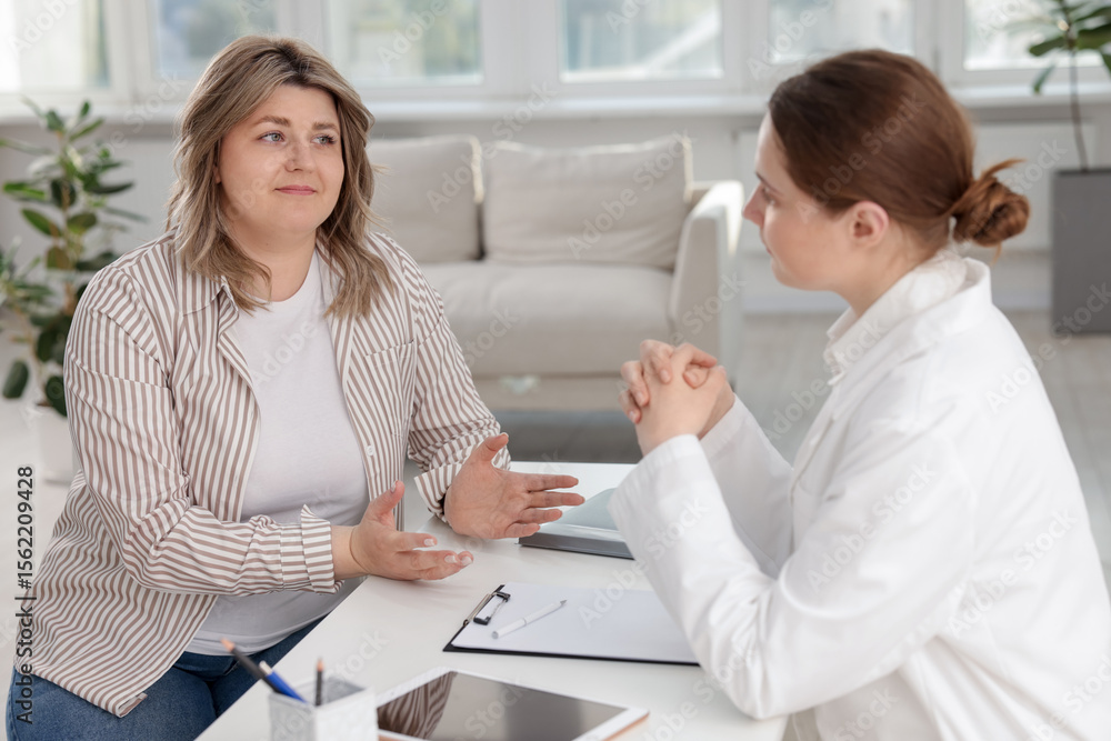 Fototapeta premium Weight loss. Nutritionist consulting overweight woman at white desk in clinic