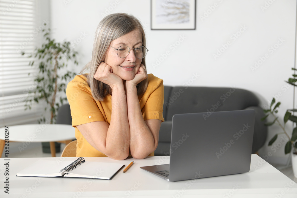 Smiling woman learning online using laptop at table indoors. Self-study