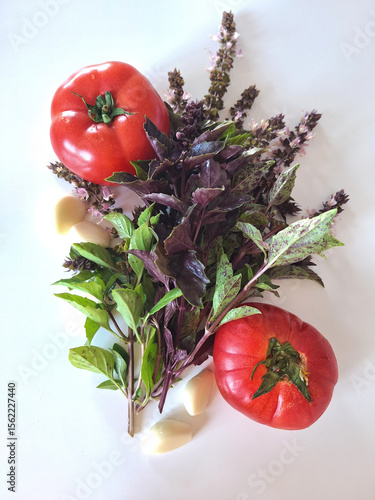 Juicy ripe red tomatoes, fresh basil and garlic cloves on a light background. Flatly. Fresh natural ingredients for cooking.