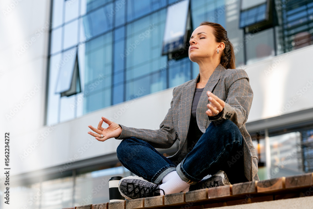 Fototapeta premium Modern urban office worker meditating during lunch break in downtown. Employee wellbeing.