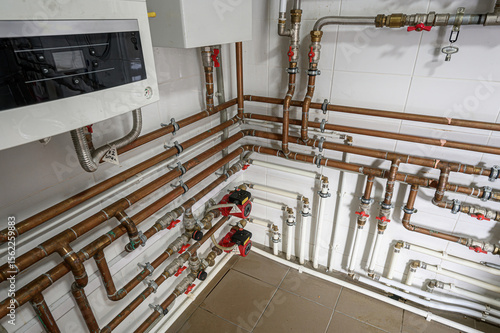 complex network of copper and white PVC pipes with valves and pumps against a tiled wall. Appears to be a mechanical or utility room