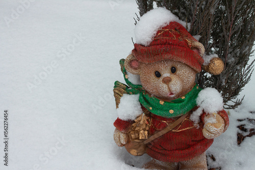 Souvenir garden figurine. A Christmas bear in a hat and scarf on the background of a winter landscape. A magical holiday scene with a place for the text. Perfect for Christmas