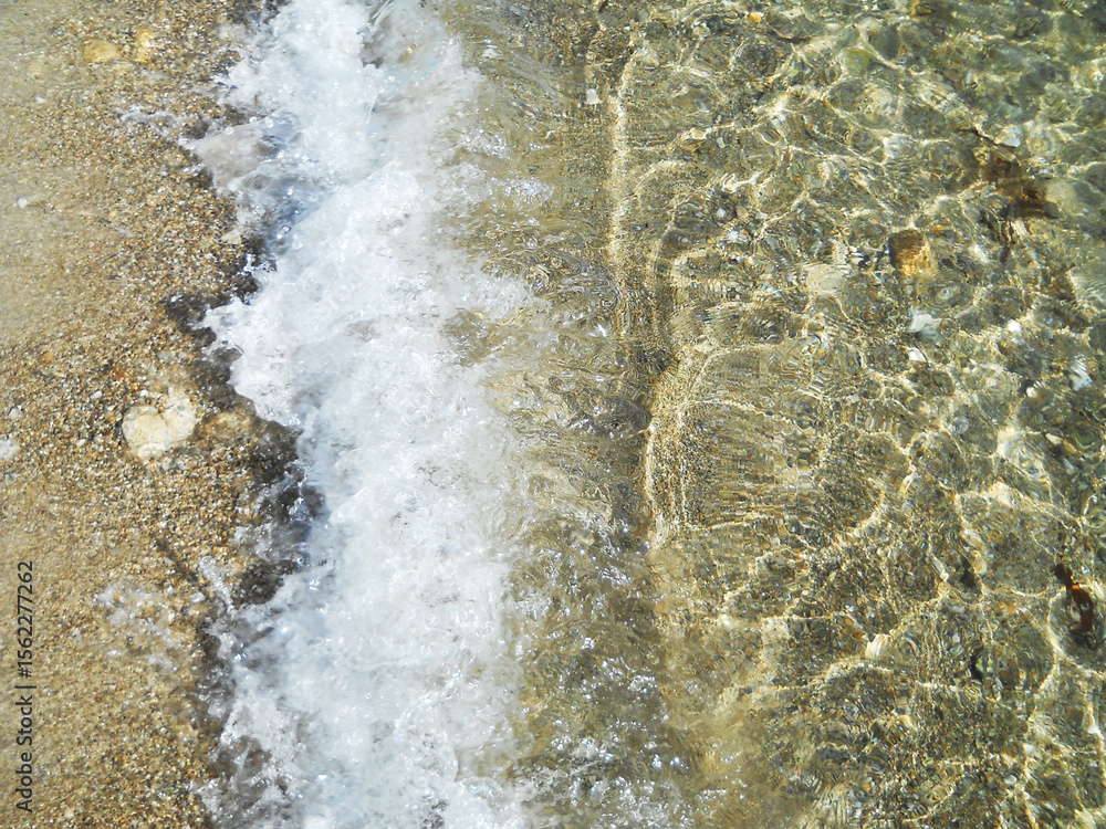 Obraz premium Close -up view of the crystal- clear, transparent sea with gentle waves and white foam off the coast of Sardinia, Italy. The pristine Mediterranean sea.