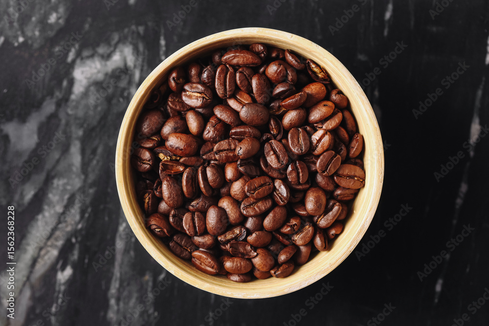 Fototapeta premium Roasted coffee beans in bowl. Brown aromatic grains on black marble. Fresh caffeine source. Natural organic drink ingredient. Morning energy concept. Minimal food flatlay for coffee lovers.