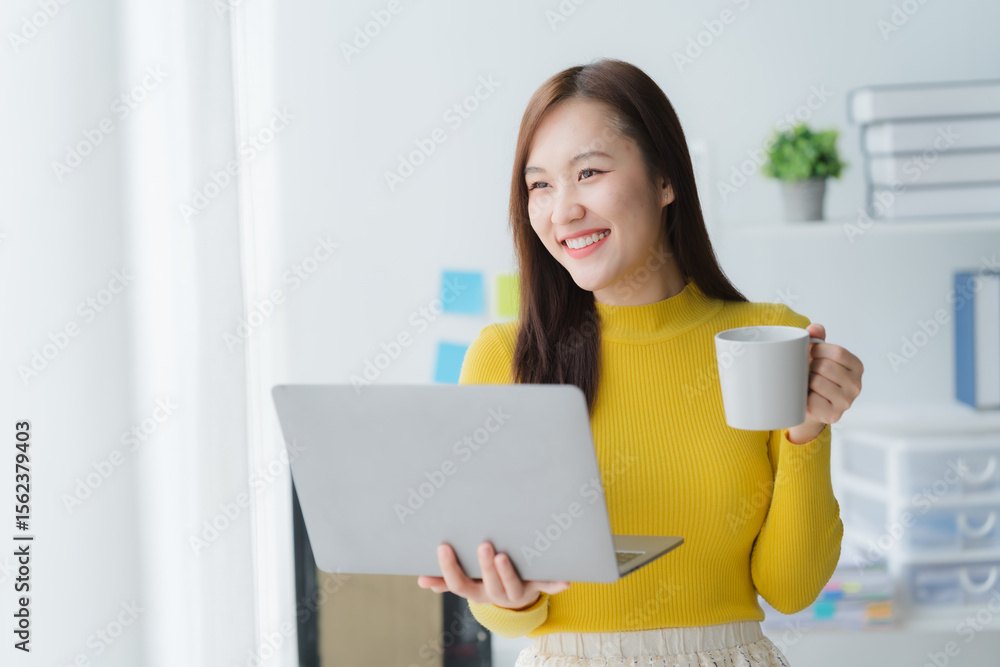 Serene Workspace: An asian woman finds contentment in her light-filled workspace, sipping from a mug, laptop close, the day's goals align with ease and happiness Serene Workspace: An asian woman finds contentment in her light-filled workspace, sipping from a mug, laptop close, the day's goals align with ease and happiness