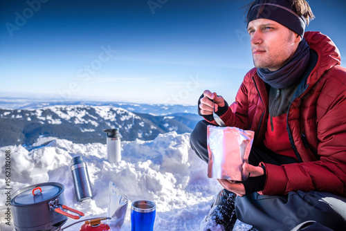 Man eating freeze-dried meal while winter camping in snowy mountain landscape