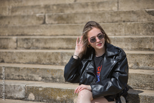 Photography Young, beautiful, blonde woman in leather jacket, snake miniskirt and sunglasses, pensive and worried, sitting on stairs