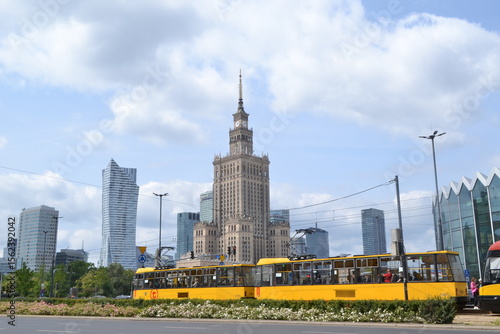 Iconic Palace of Culture and Science Dominating the Skyline of Warsaw, Poland, with Modern Skyscrapers and a Bright Yellow Tram on a Sunny Day