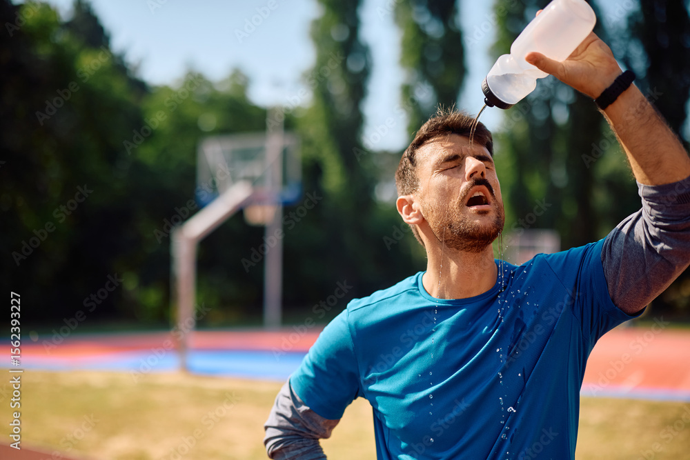 Fototapeta premium Athletic man refreshing himself with fresh water while working out outdoors.
