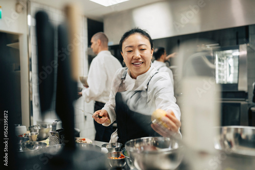 Smiling female head chef reaching for grabbing vegetable while working in restaurant kitchen