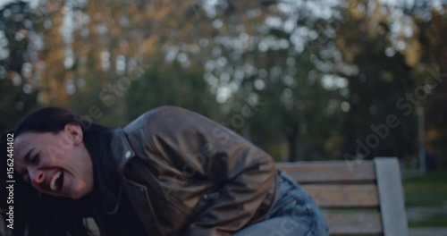 A young woman in a park displays a powerful emotional journey, transitioning from uncontrollable laughter and joy to profound sadness and crying while sitting on a bench.