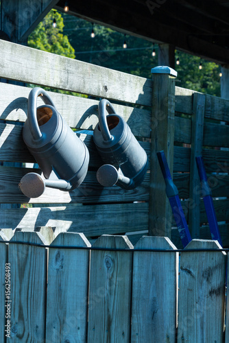 Two Watering Cans Hanging on A Fence 