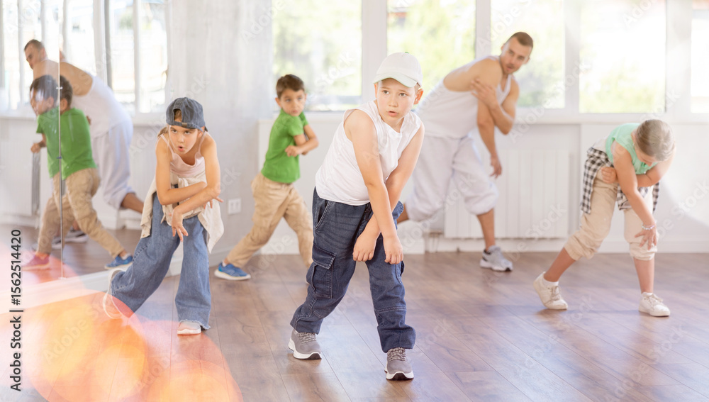 Fototapeta premium Preteen boy performing hip hop dance moves, showcasing skills and concentration, during group class for kids led by young male instructor in street dance studio