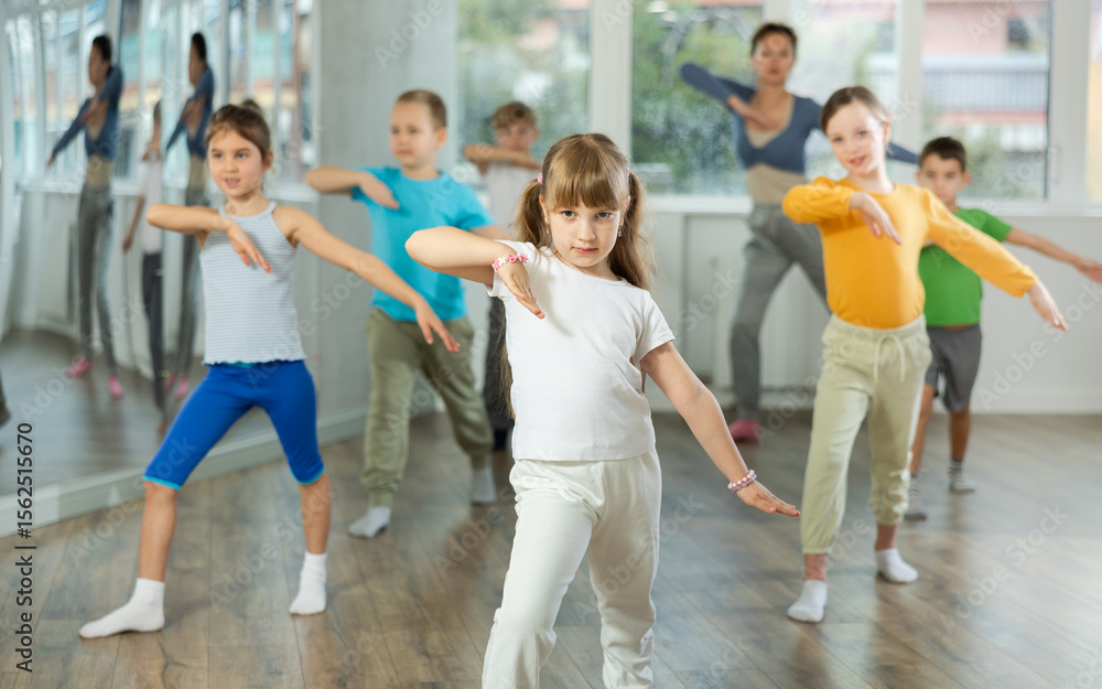 Obraz premium Girl learns to dance during childrens master class in studio. Teacher watches students, participates in training in background