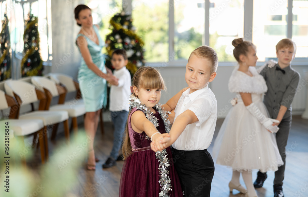 Obraz premium Joyful minor schoolboys and schoolgirls training valse dance in events salon adorned with Xmas tree