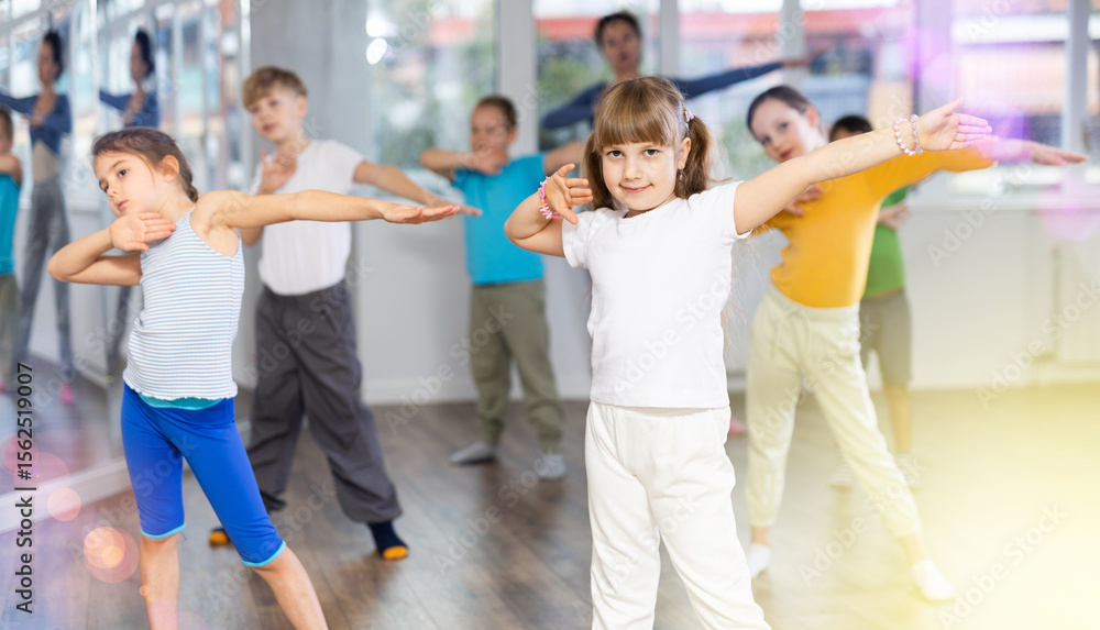 Fototapeta premium Dynamic little girl training hip hop dance poses with instructor and other attendees of dancing courses