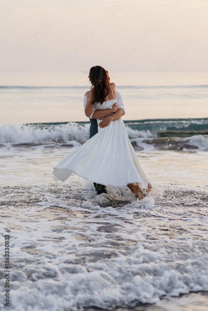 Romantic couple embracing in ocean waves at sunset during honeymoon Romantic couple embracing in ocean waves at sunset during honeymoon