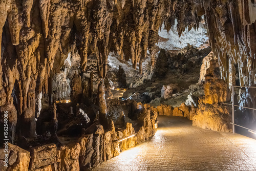 Stalactites hanging from ceiling in illuminated cave with walking path, Skocjan cave, Slovenia