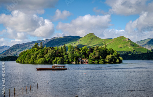 A serene morning view of Derwentwater Lake with Derwent Isle and Catbells fell in the frame, as a ferry boat crosses the water, bathed in soft summer sidelights 2
