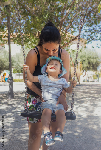 Enjoying a sunny day at the park, a mother pushes her smiling child on a swing