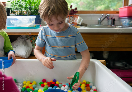 Child works gross motor skills, using tweezers at sensory table
