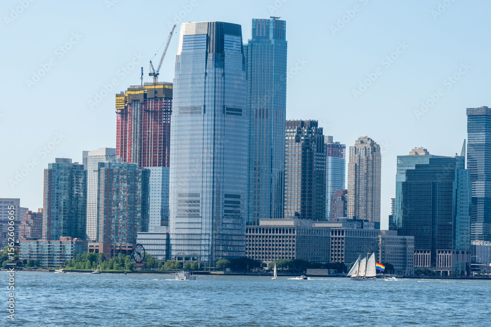Fototapeta premium City skyline featuring skyscrapers and boats on the water. Clear blue sky provides backdrop for urban landscape with boats on the water in foreground.