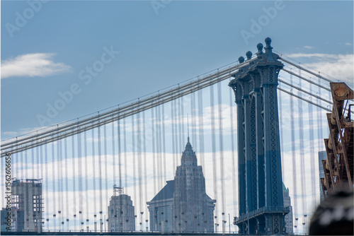 Obraz na plátně An eye-level shot showing a bridge with wires and a blue sky, with buildings visible between the wires and bridge structures, giving a scenic view
