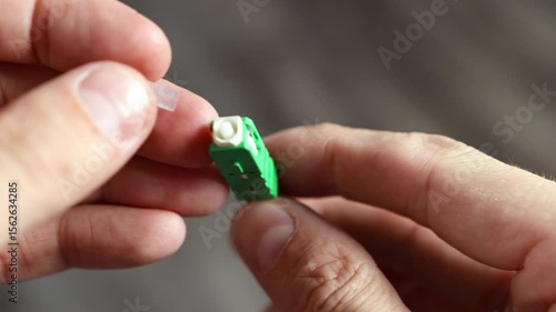 Demonstration of an APC fiber optic connector connected to a cable, showing rotation and opening of the protective cap where light passes through 