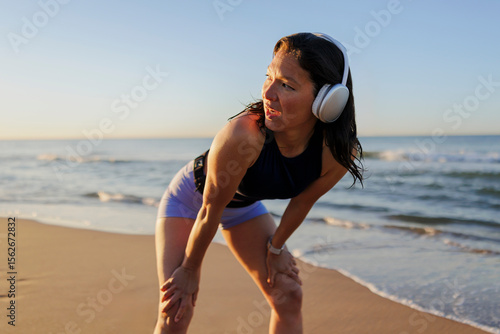 Tired sportswoman catching her breath after running workout on beach
