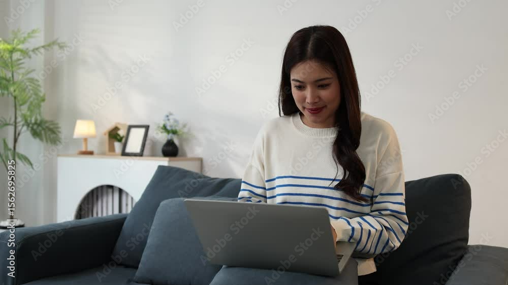 A woman is sitting on the sofa playing with her laptop, she is relaxing on her day off doing activities in the living room, she is using her laptop to play social media and chat with her friends. A woman is sitting on the sofa playing with her laptop, she is relaxing on her day off doing activities in the living room, she is using her laptop to play social media and chat with her friends.