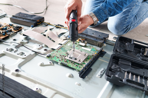 Technician repairing circuit board of a big led tv with an electric screwdriver