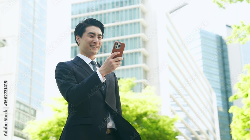 新緑の街でスマホを使う男性ビジネスパーソン 新緑の街でスマホを使う男性ビジネスパーソン