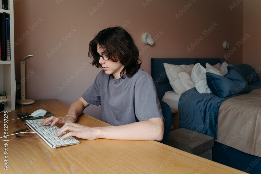 Teen Focuses Intensely While Working at a Desk in Cozy Bedroom Teen Focuses Intensely While Working at a Desk in Cozy Bedroom