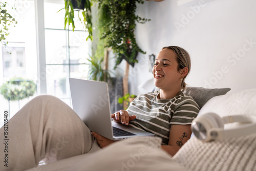 Young woman working from home laying on bed using laptop