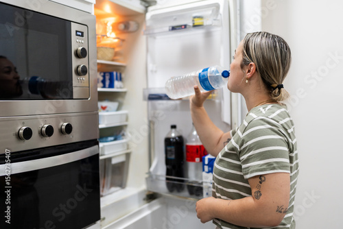 Woman drinking fresh water directly from the bottle in the kitchen