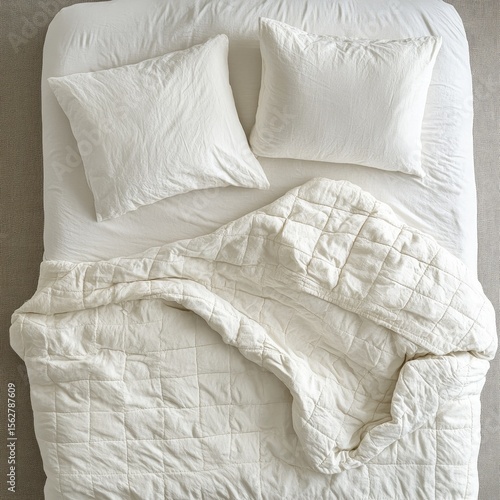 A meticulously arranged, ivory-toned bed set.  Two matching pillows rest on a crisp, white bed sheet.  A quilted, ivory comforter is draped over the bed