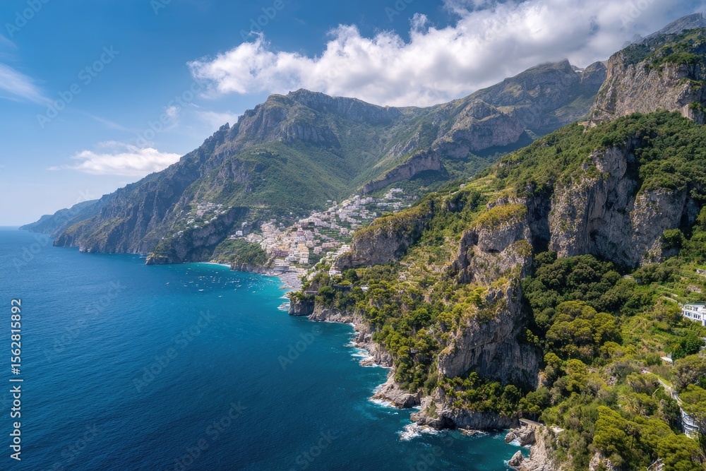 Fototapeta premium A coastal town nestled between lush, verdant mountains and a deep blue sea under a partly cloudy sky