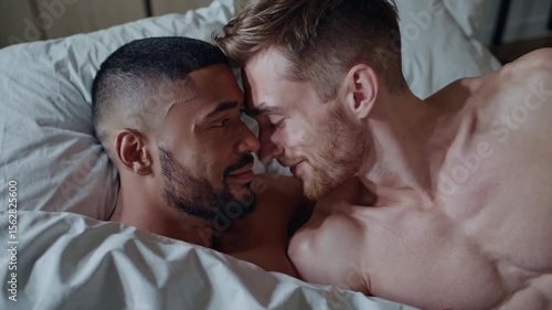 Loving gay men couple in morning embrace smiling in bed