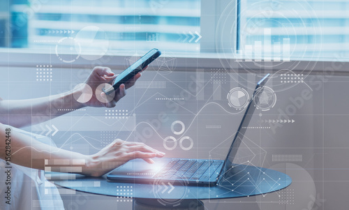 ビジネスシーン、スマホとノートパソコンを操作する女性、スマホで検索するイメージ、IT企業、オフィスワーク、デジタルネットワークイメージ