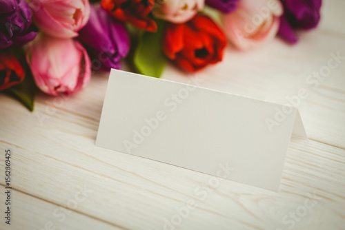 Fototapeta Naklejka Na Ścianę i Meble -  folded white place card is sitting on whitewashed tabletop, showing colorful tulip bouquet backdrop