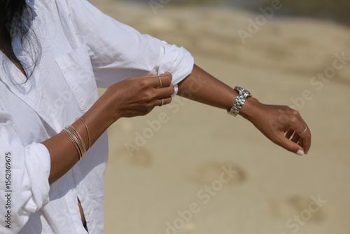 Woman with Black Hair Rolling Up Sleeve of White Shirt on the Beach