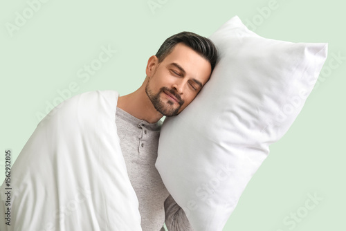 Handsome man with soft pillow and blanket sleeping on green background