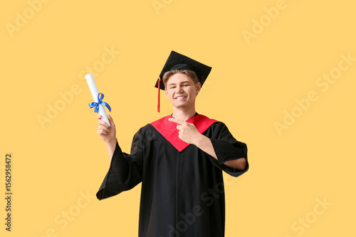 Happy male graduate pointing at diploma on yellow background