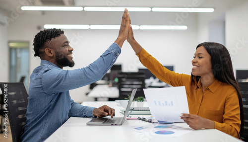 Coworkers high-fiving after successfully completing a big project, with charts and laptops in the background