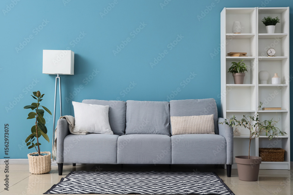 Fototapeta premium Comfortable sofa, houseplant and shelving unit near blue wall in room