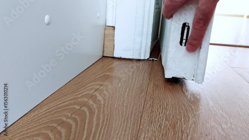 Hands inspect a floor-mounted door lock-fingers test the latch and alignment, capturing a close-up moment of tactile focus and quiet home security attention