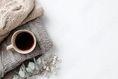 Cozy autumn scene a cup of coffee rests atop folded knit sweaters, alongside eucalyptus and baby's breath, on a white background