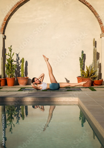 atletic young woman in pilates pose on mat near swimming pool